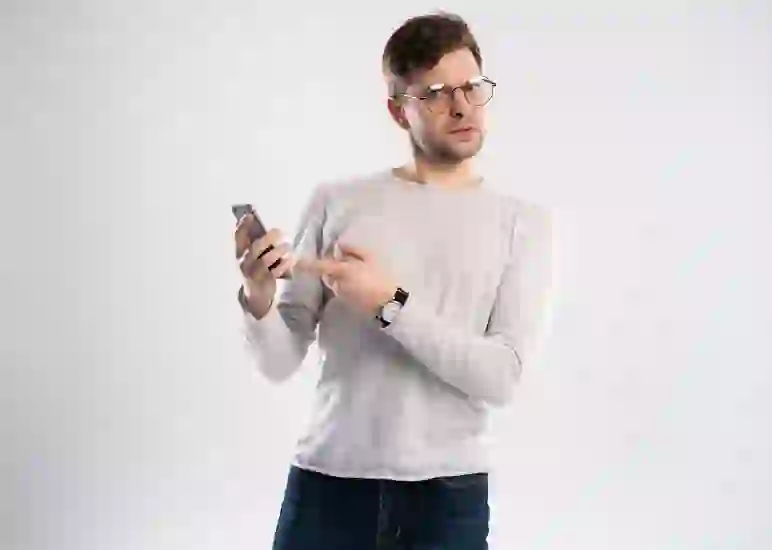 man with glasses points questioningly at his cellphone