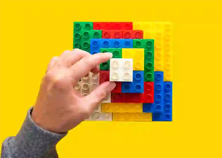 a hand placing legos against a yellow background